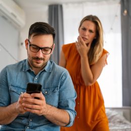 Jealous woman looking on as man uses cell phone while sitting