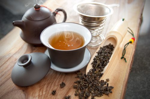 black teapot, cup of oolong tea, and oolong tea leaves displayed on a wood board