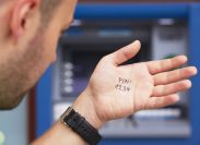 closeup of a man looking at the palm of his hand with "pin 1234" written on it, standing in front of an ATM.