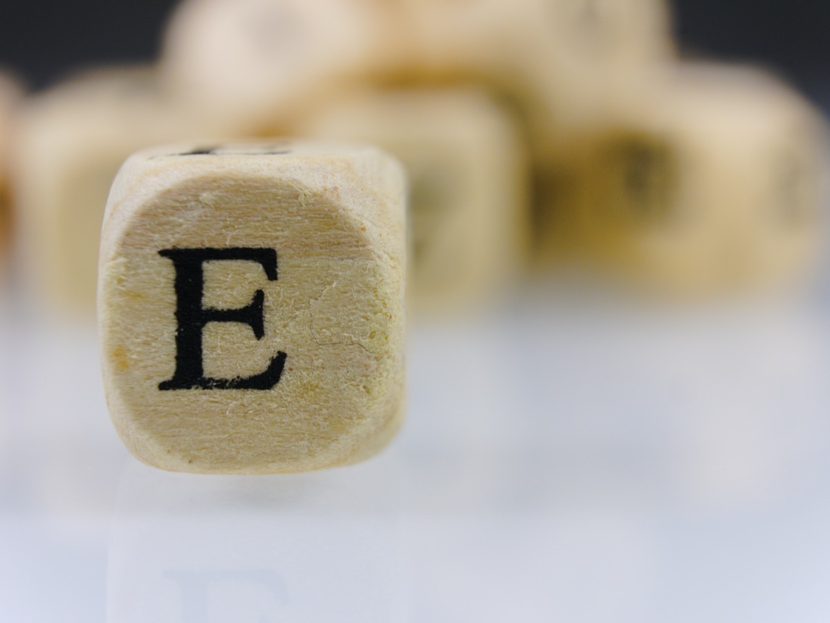 The letter E on a wooden cube with other dice letters in the background