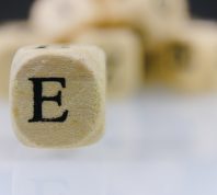 The letter E on a wooden cube with other dice letters in the background