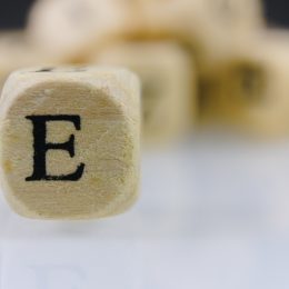 The letter E on a wooden cube with other dice letters in the background