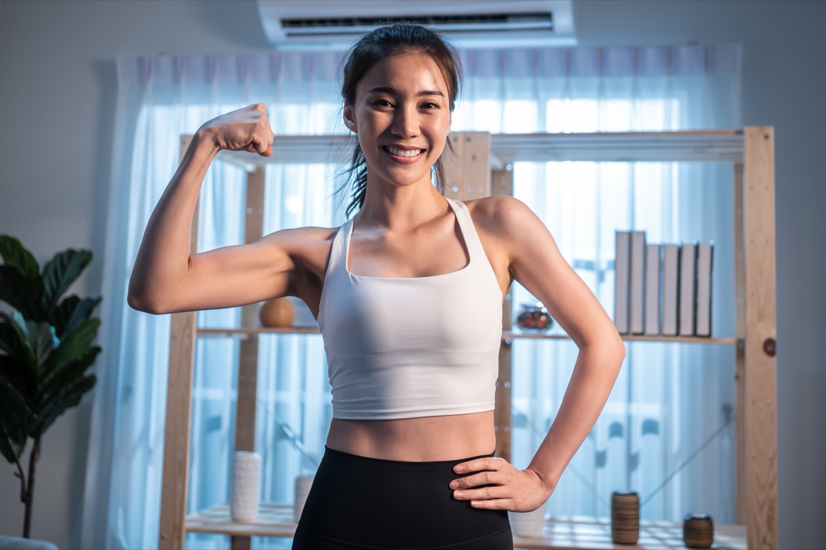 Portrait of Asian active young girl in sportswear stand crossing arms. Attractive beautiful women with six packs abs look at camera and smile after exercise or yoga, Spend time leisure in living room.