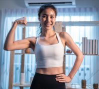 Portrait of Asian active young girl in sportswear stand crossing arms. Attractive beautiful women with six packs abs look at camera and smile after exercise or yoga, Spend time leisure in living room.