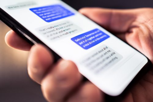 man holding phone in his hand with blurred text conversation on screen
