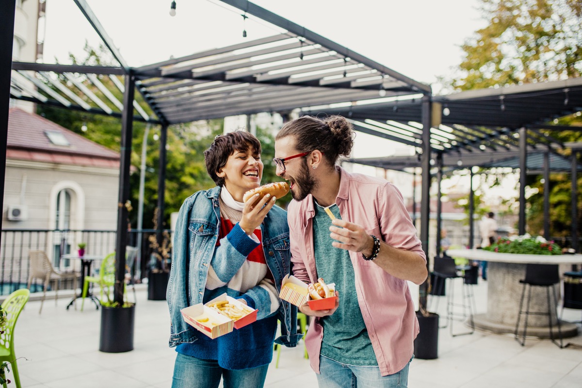 Young couple is eating hot dog outdoors and having fun
