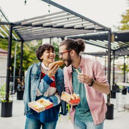 Young couple is eating hot dog outdoors and having fun