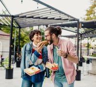 Young couple is eating hot dog outdoors and having fun