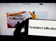 Person holding smartphone with logo of French e-commerce company Vestiaire Collective SA on screen in front of website.