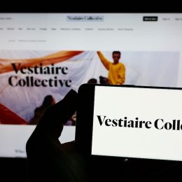Person holding smartphone with logo of French e-commerce company Vestiaire Collective SA on screen in front of website.