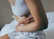 Menstruation, sick and stomach ache with black woman in bedroom for indigestion, cramps and illness. Frustrated, gas and stress with girl on bed for constipation, bloating and intestine problems