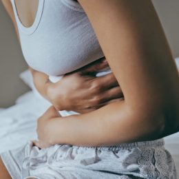 Menstruation, sick and stomach ache with black woman in bedroom for indigestion, cramps and illness. Frustrated, gas and stress with girl on bed for constipation, bloating and intestine problems