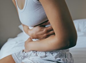 Menstruation, sick and stomach ache with black woman in bedroom for indigestion, cramps and illness. Frustrated, gas and stress with girl on bed for constipation, bloating and intestine problems
