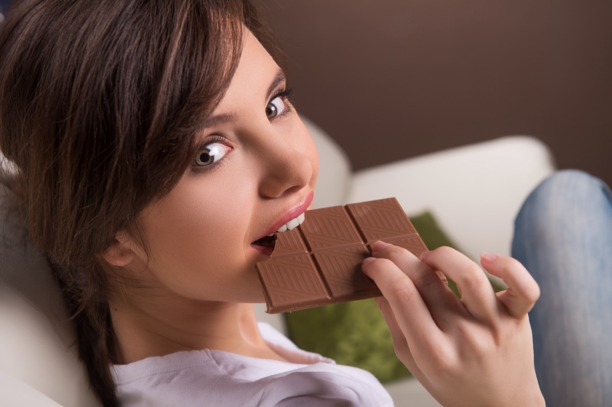 Woman eating chocolate. Beautiful young woman sitting on the coach and eating chocolate