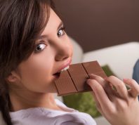 Woman eating chocolate. Beautiful young woman sitting on the coach and eating chocolate