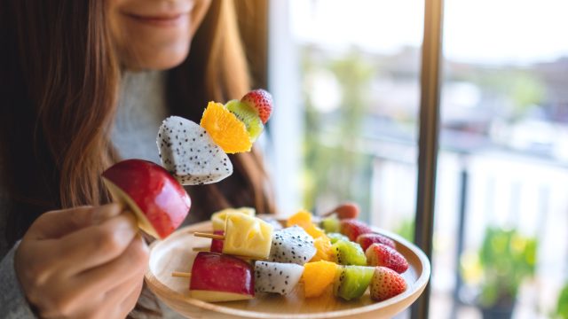 A close up of a person eating fruit skewers