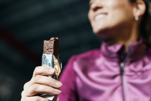 Close up of woman wearing a purple jacket eating a protein bar