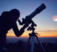 Woman looking at night sky with amateur astronomical telescope.