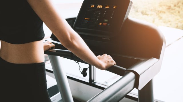 Woman wearing black workout clothes on a treadmill looking at stats on the screen