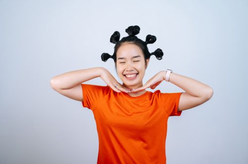 portrait of a young woman wearing an orange t-shirt with her hair in many small buns on a gray background