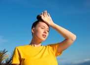 overheated young woman wearing a yellow shirt and putting a hand on her head in the sun