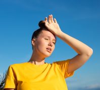 overheated young woman wearing a yellow shirt and putting a hand on her head in the sun