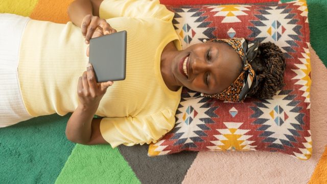 A woman lying down and reading a Kindle e-reader