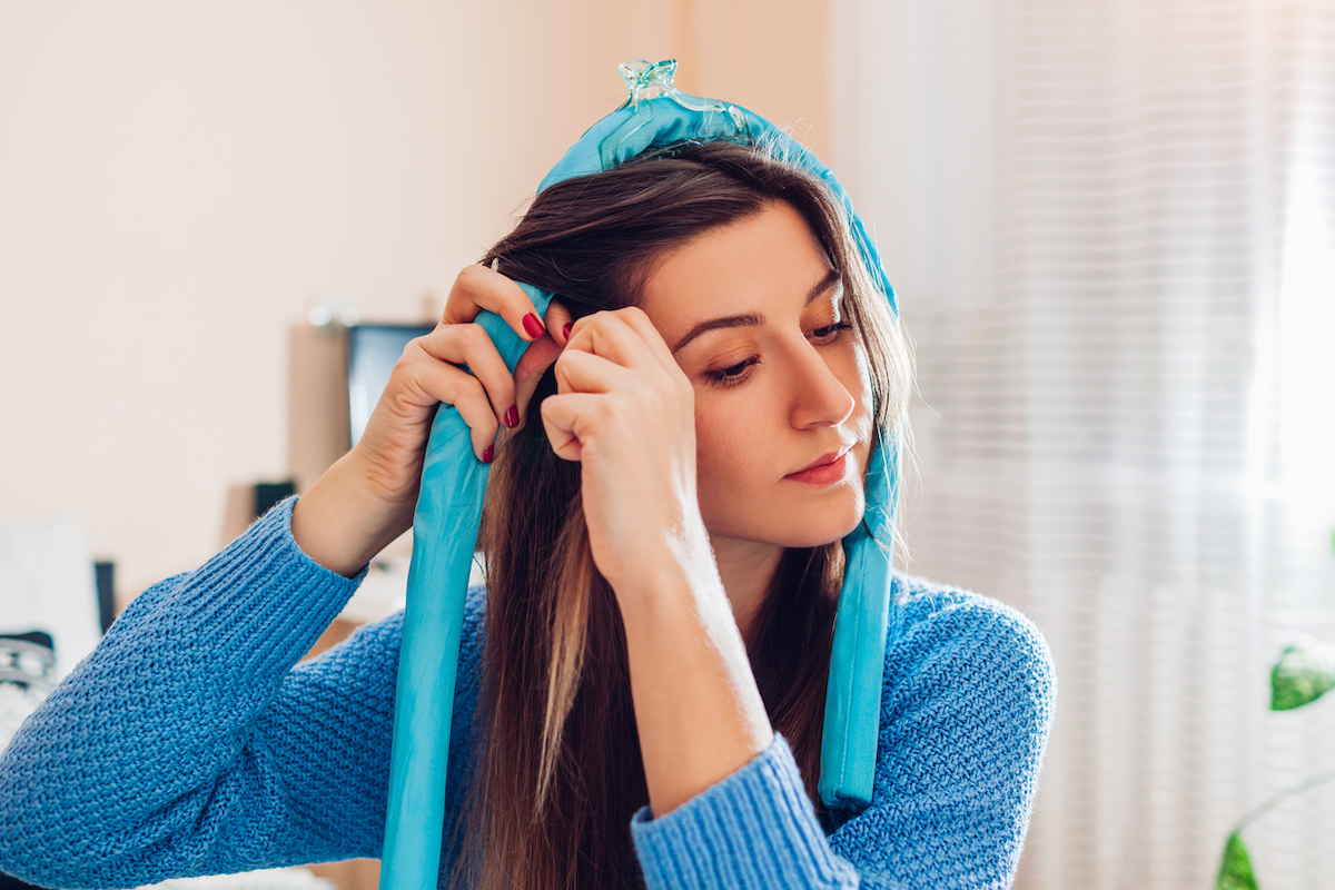 woman in a blue sweater putting a blue heatless hair curler in her hair