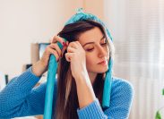 woman in a blue sweater putting a blue heatless hair curler in her hair