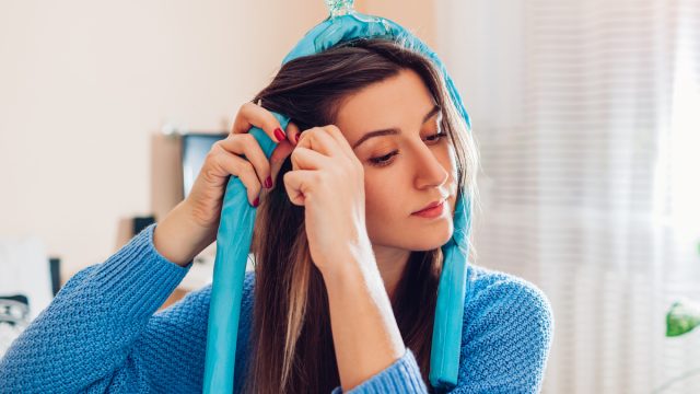 woman in a blue sweater putting a blue heatless hair curler in her hair