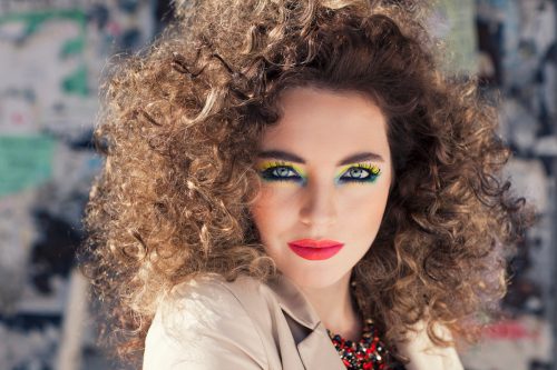 Young beautiful model with bright make-up standing on the street girl with expressive make-up and curly hair.