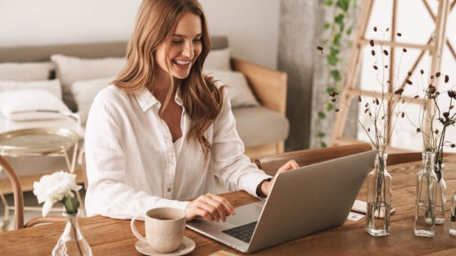 woman smiling while working on her laptop on a table with coffee