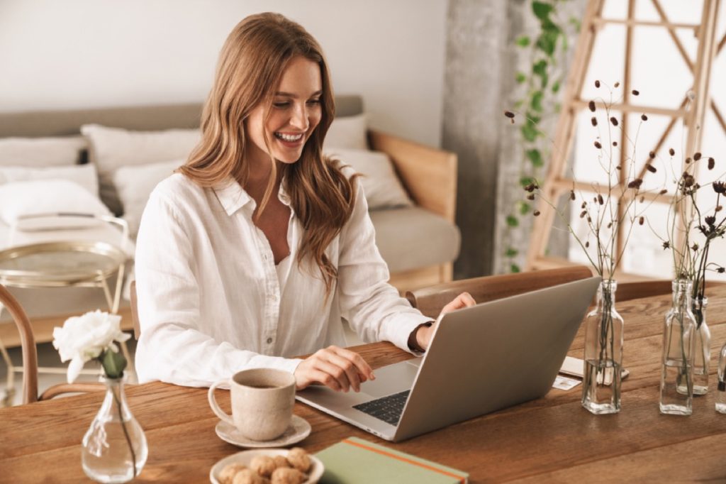 woman smiling while working on her laptop on a table with coffee