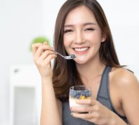 Healthy Diet And Nutrition. Portrait of happy beautiful young Asian woman eating natural yogurt at home and looking at camera.Weight Loss Food Concept. High Resolution