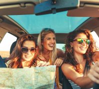 Three women in a car smiling while checking a map