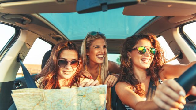Three women in a car smiling while checking a map