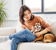 happy young woman holding her dog on the couch