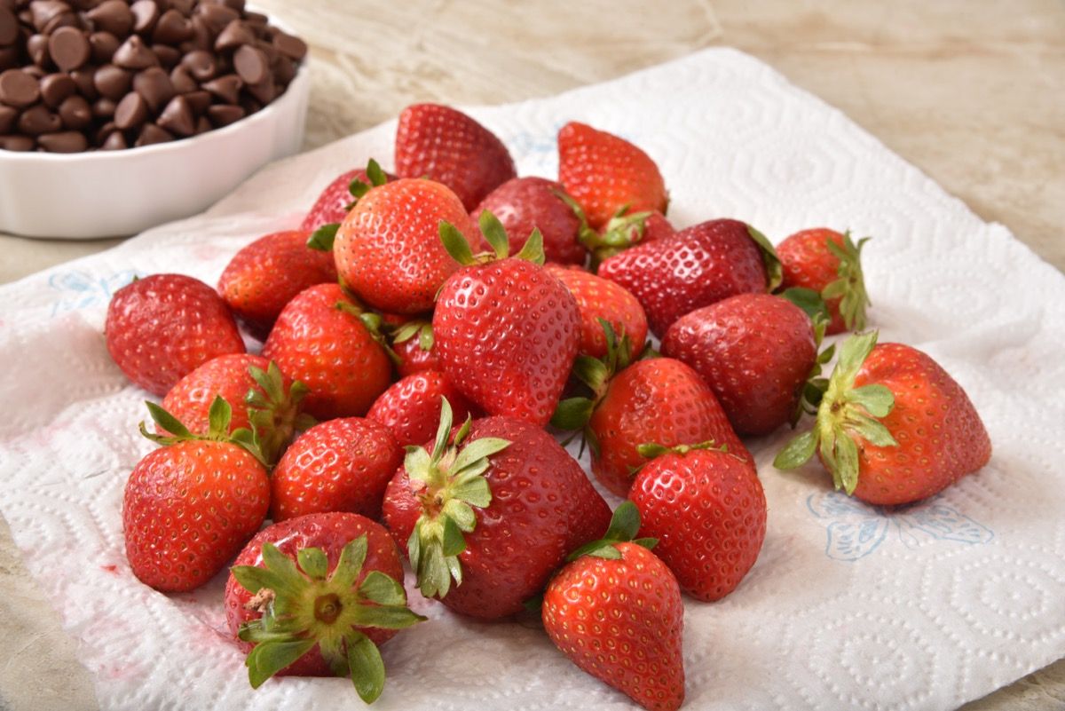 Fresh ripe strawberries drying on a paper towel next to a bowl of chocolate chips