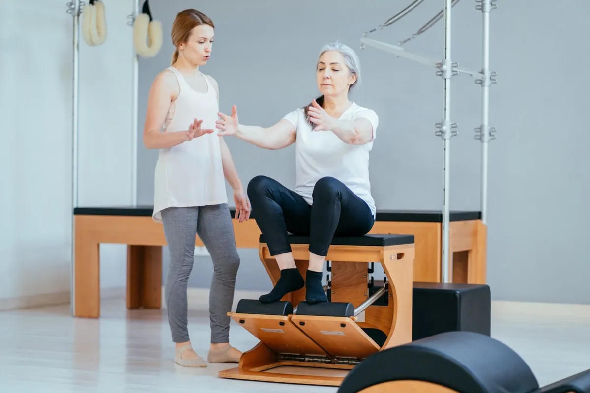 Woman doing chair pilates with the help of a young female trainer