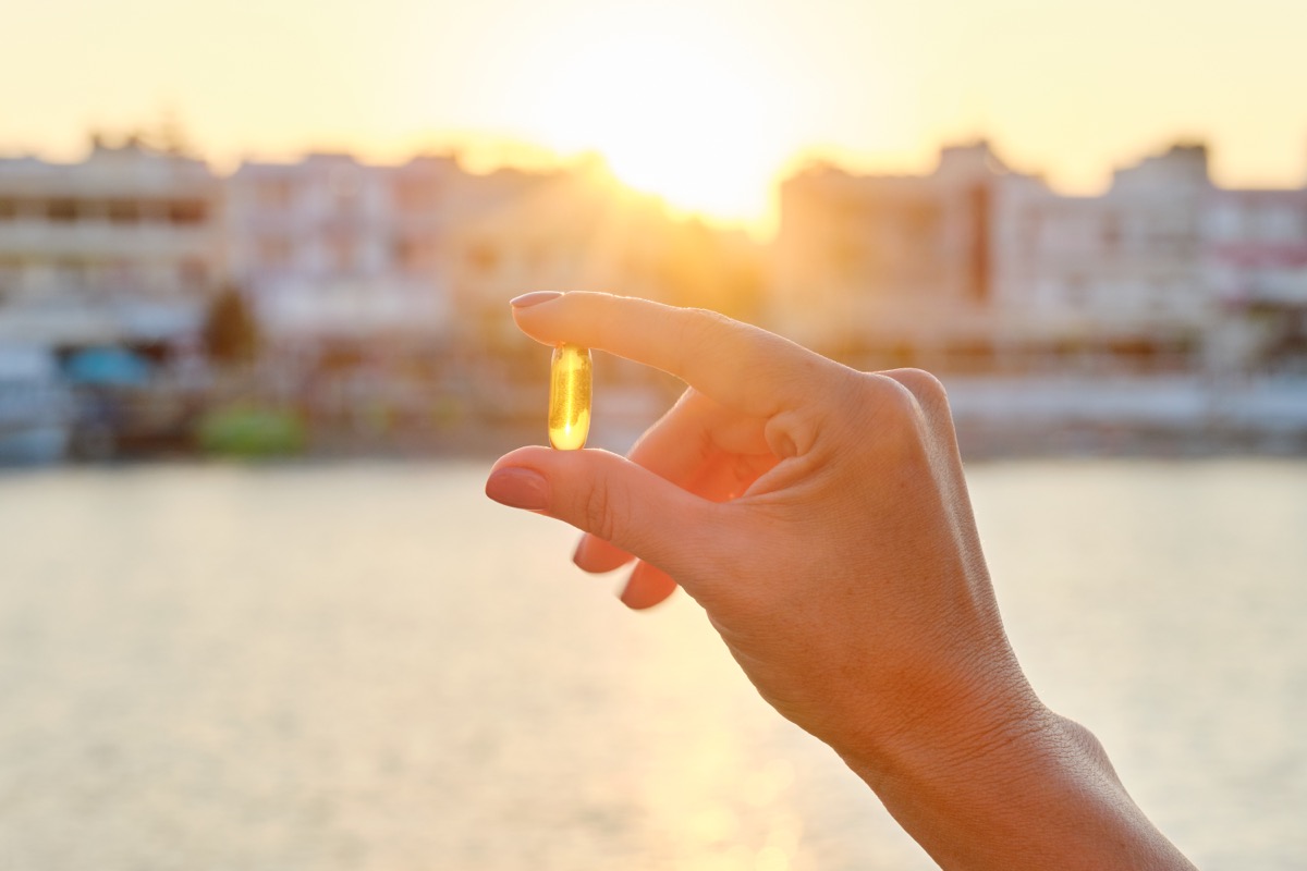 Yellow vitamin gel capsule in woman's hand, sun sea background.