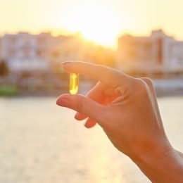 Yellow gel capsule vitamin d omega-3 in womans hand, sun sea background.