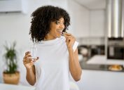 Happy woman in a white t-shirt takes a supplement with a glass of water in her kitchen
