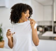 Happy woman in a white t-shirt takes a supplement with a glass of water in her kitchen