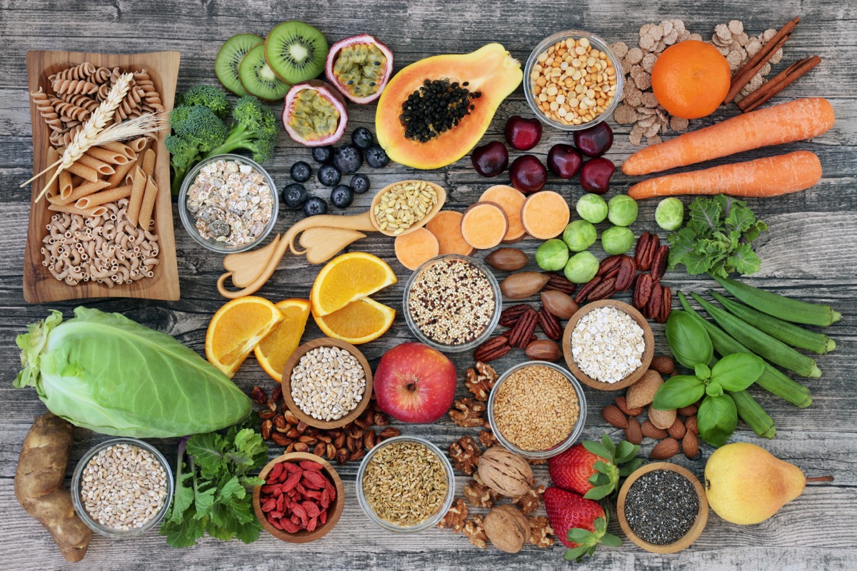 high-fiber foods on a wood table with fruit, vegetables, whole wheat pasta, legumes, cereals, nuts and seeds