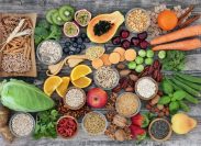 high-fiber foods on a wood table with fruit, vegetables, whole wheat pasta, legumes, cereals, nuts and seeds