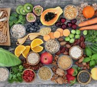 high-fiber foods on a wood table with fruit, vegetables, whole wheat pasta, legumes, cereals, nuts and seeds