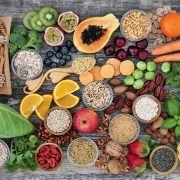 high-fiber foods on a wood table with fruit, vegetables, whole wheat pasta, legumes, cereals, nuts and seeds