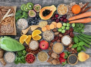 high-fiber foods on a wood table with fruit, vegetables, whole wheat pasta, legumes, cereals, nuts and seeds