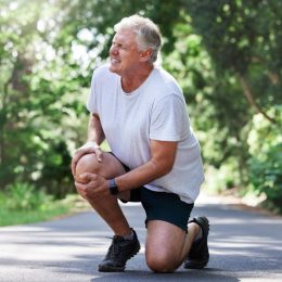 Running, injury and old man with knee pain on path in nature for outdoor fitness and workout exercise. Health, wellness and muscle strain, senior runner with hand on leg in support or relief for ache