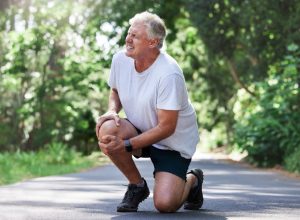 Running, injury and old man with knee pain on path in nature for outdoor fitness and workout exercise. Health, wellness and muscle strain, senior runner with hand on leg in support or relief for ache